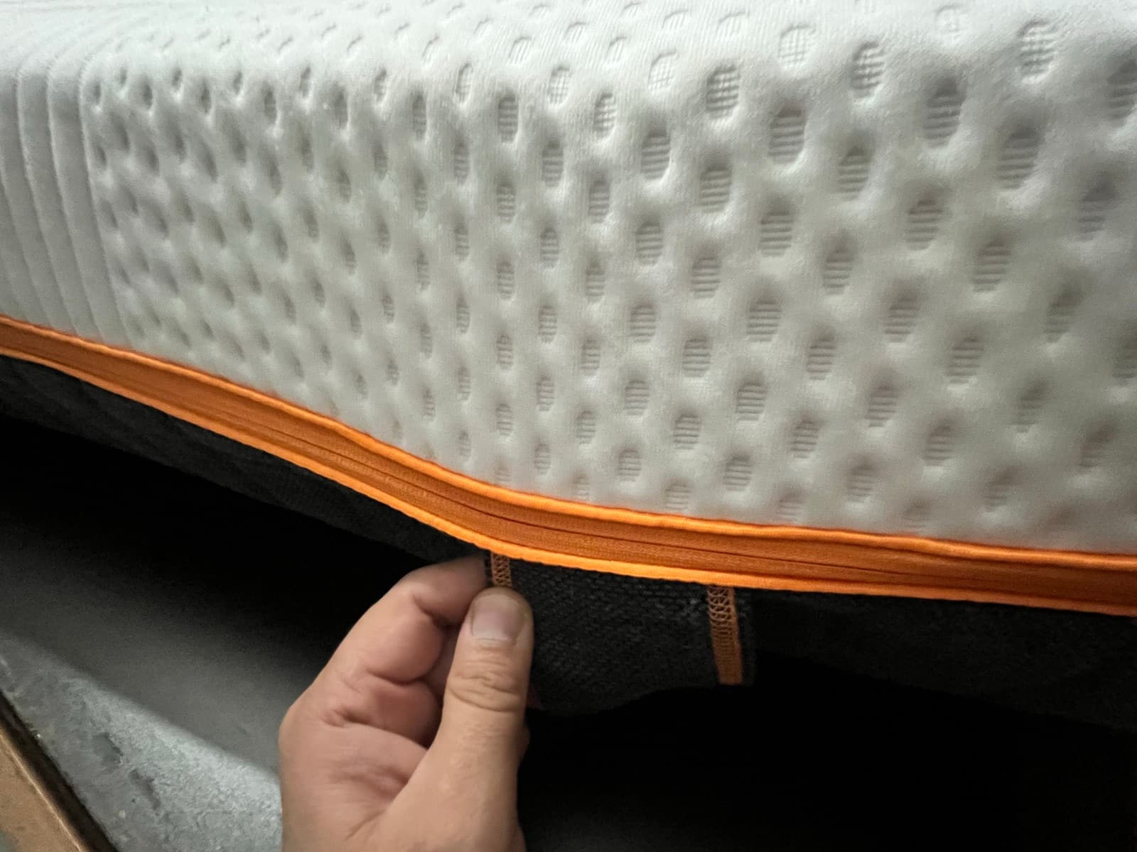 A hand gripping the side carry handle, with the mattress's orange trim and dark side panel.